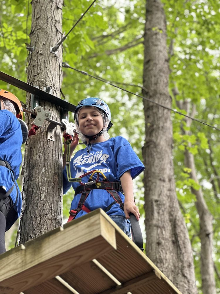 Child in a blue shirt and helmet standing on a platform among trees.