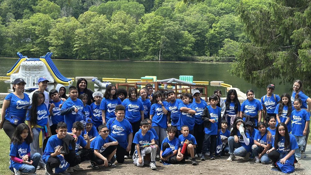 Large group of children in blue shirts posing by a lake.