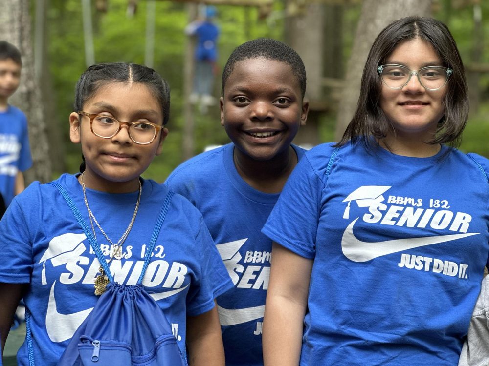 Three children in blue shirts smiling together at a park.
