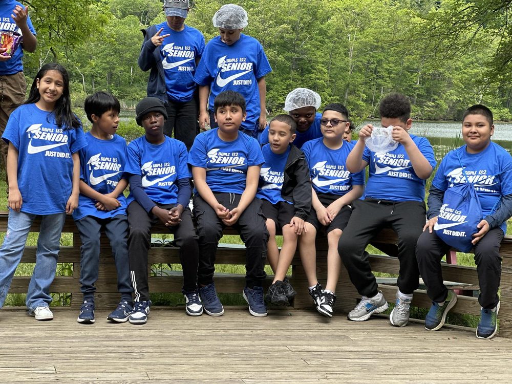 Group of children in blue shirts posing on a wooden platform in a forest.