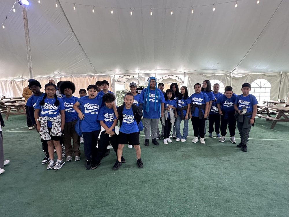 Large group of children in blue shirts inside a tent with picnic tables.