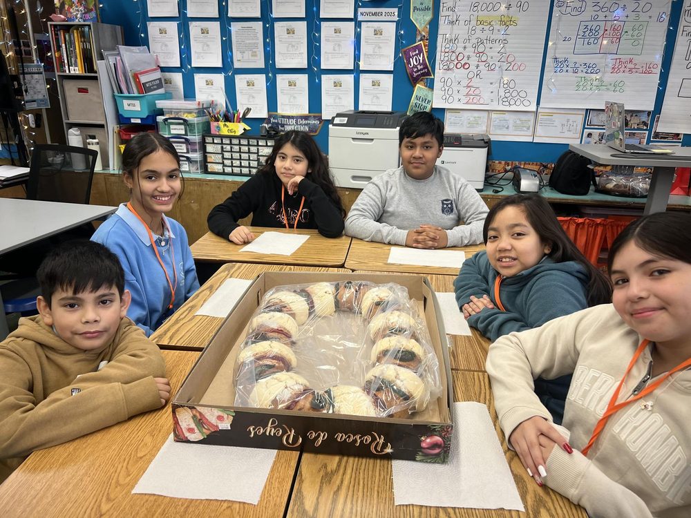 Six students sitting around a table with a decorated cake.