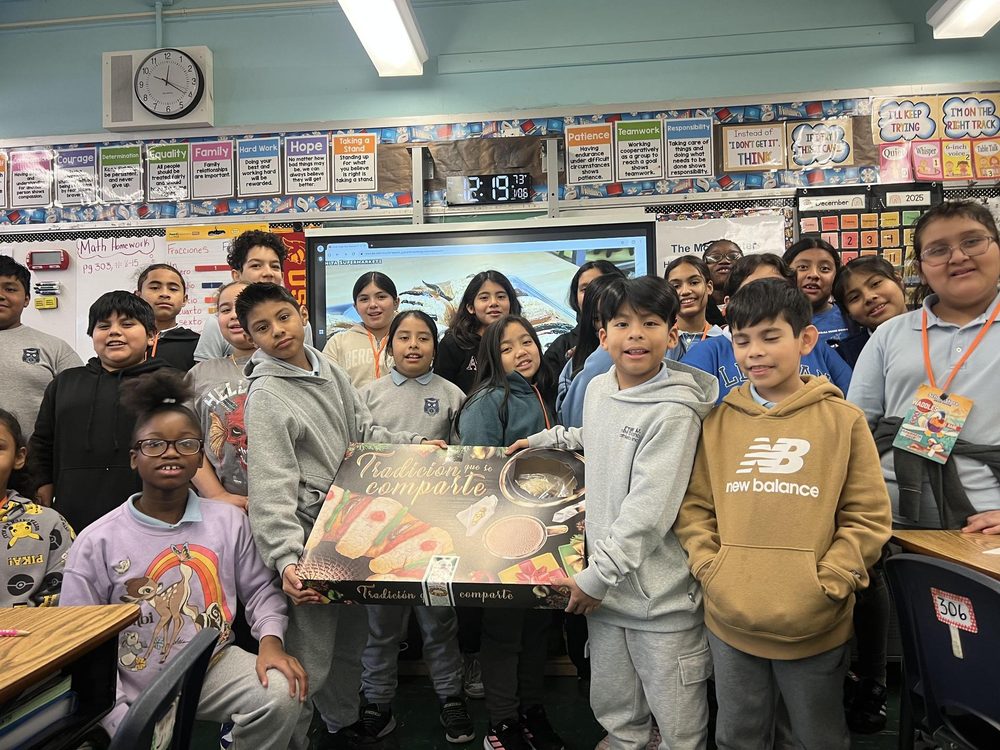 Group of students posing with a large dessert display in a classroom.